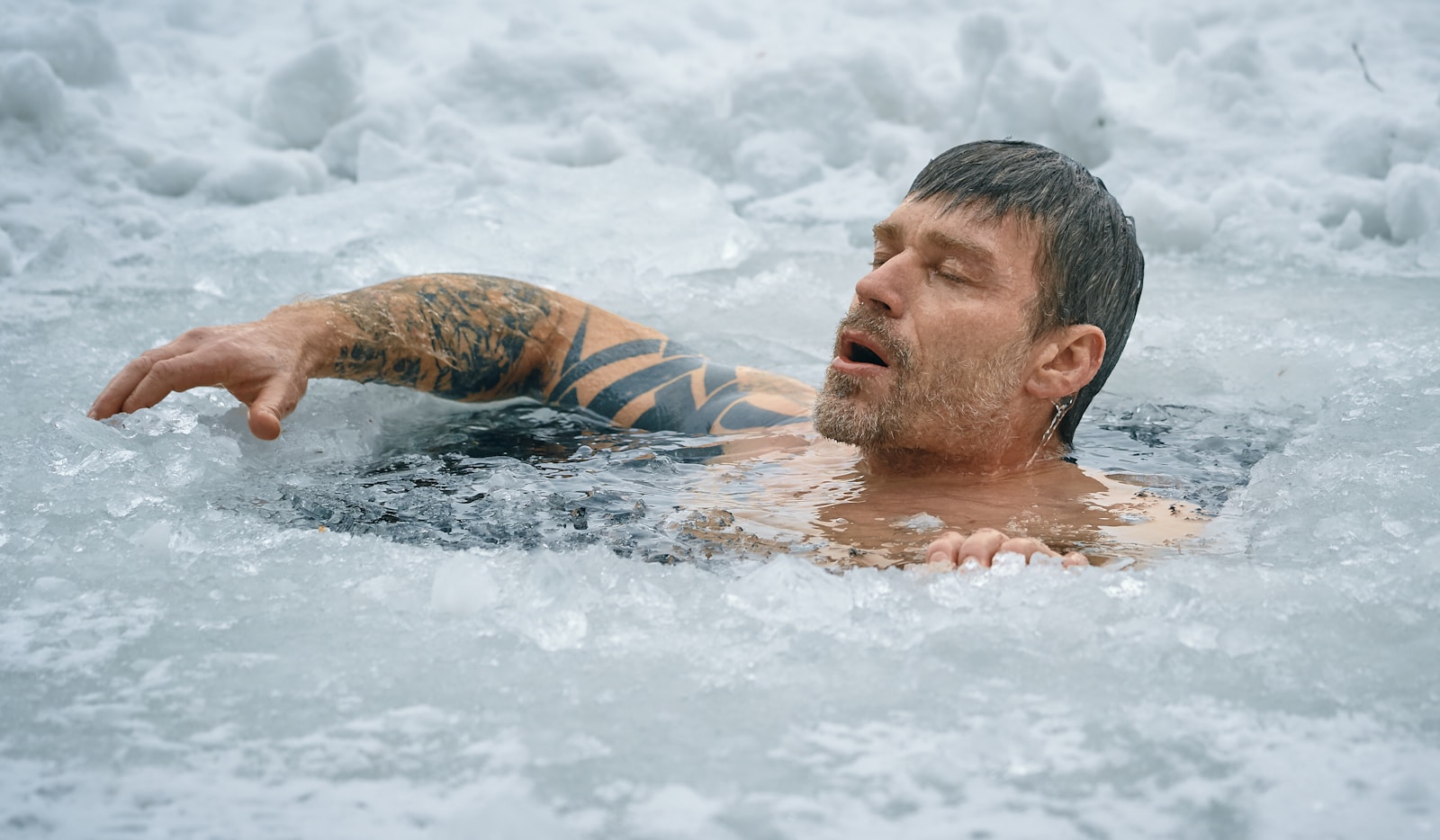 A man shoulder-deep in a hole cut through lake ice