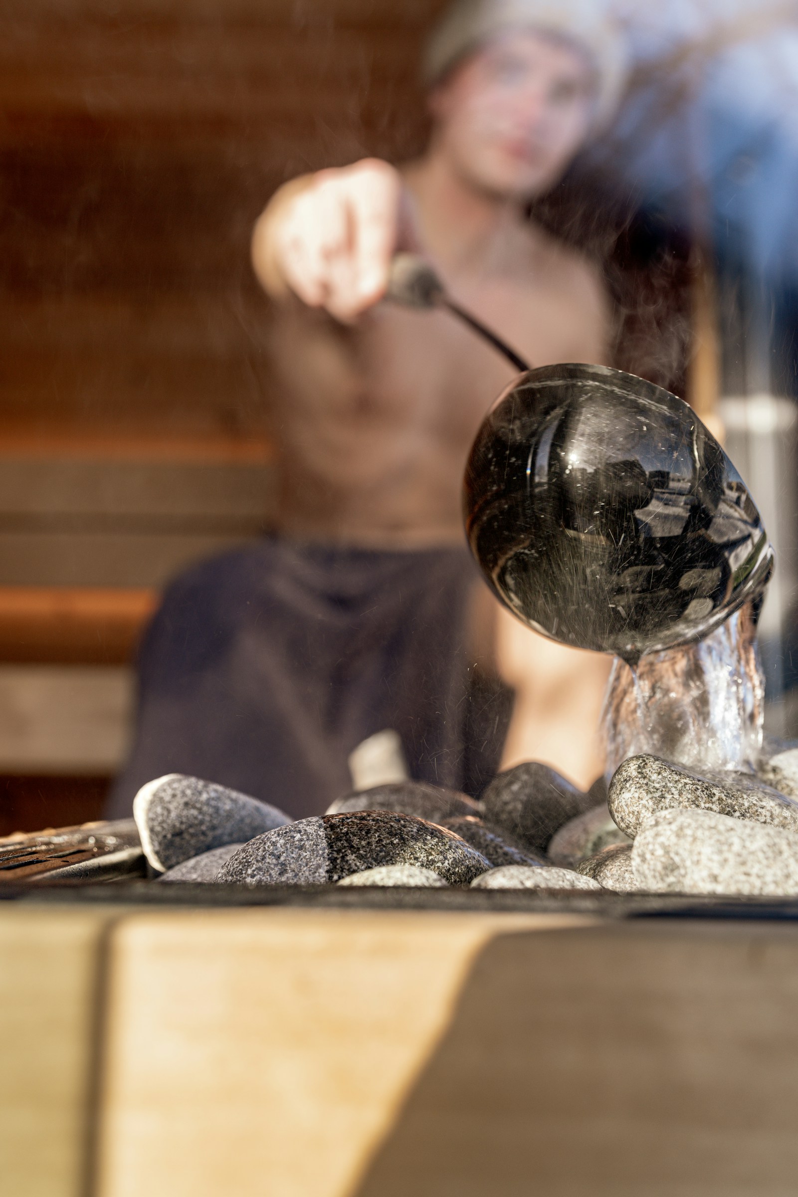 Water poured from a ladle onto hot sauna stones, steam lifting off them